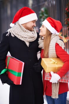Amorous couple in Santa caps and coats holding presents for Christmas