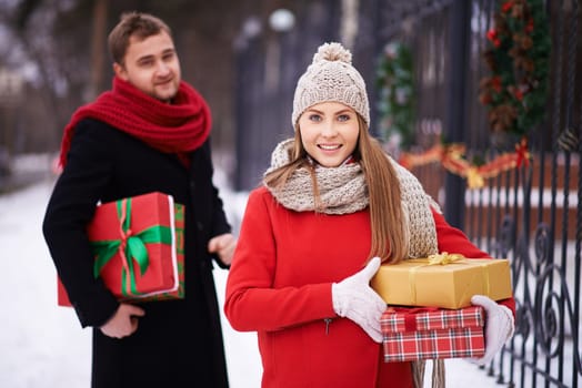 Happy woman with Christmas presents looking at camera on background of her husband outdoors