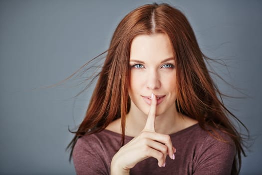 Charming female looking at camera while keeping her forefinger by lips