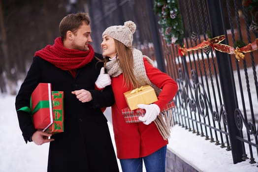 Young couple with giftboxes looking at one another while moving outdoors on Christmas eve