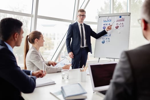 Elegant young businessman pointing at data on whiteboard during explanation of chart