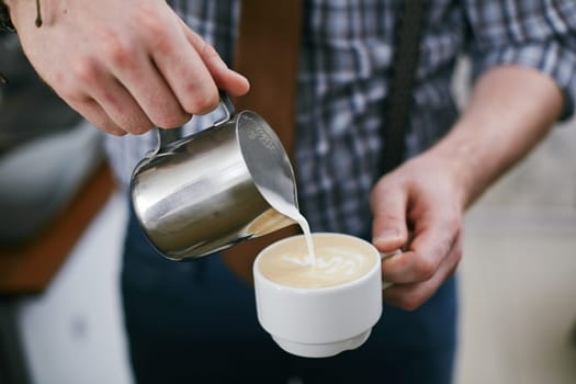 Barista pouring milk into cup of latte
