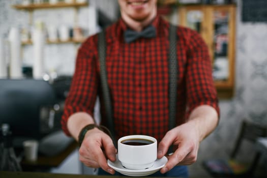 Barista holding cup of black coffee on saucer