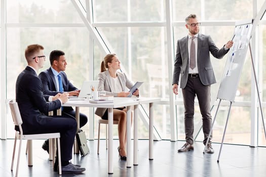 Confident businessman pointing at document on board while explaining his idea to colleagues in office