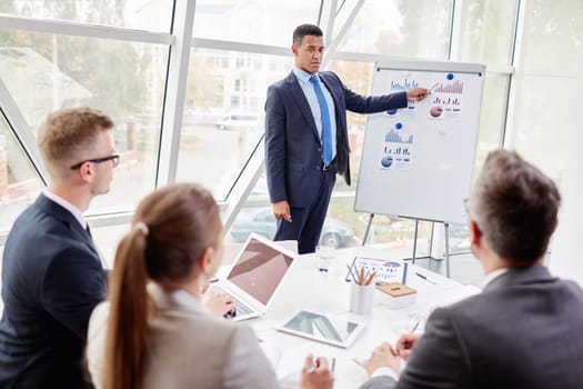 Confident businessman explaining data on board to colleagues in office