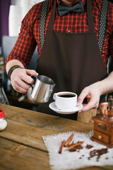 Barista in uniform holding cup black coffee and steel mug