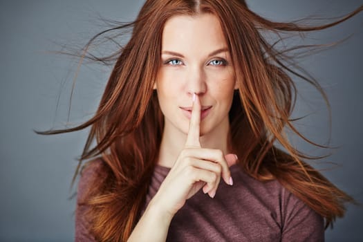 Pretty woman with her forefinger by mouth looking at camera