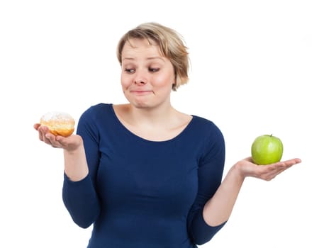 Young woman holding a donut and an apple and being more attracted by the donut, isolated on white