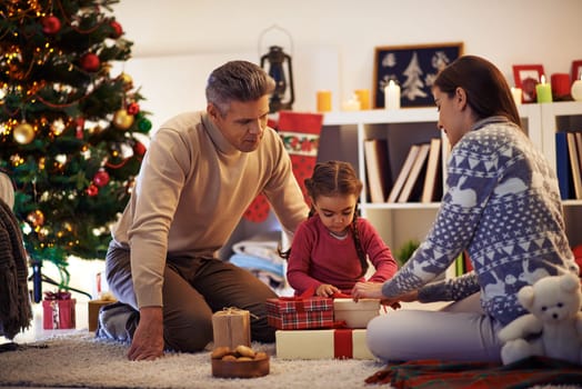 Family of three packing gifts and tying knots on tops of boxes before Christmas
