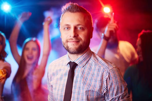 Handsome man looking at camera at party on background of dancing freinds
