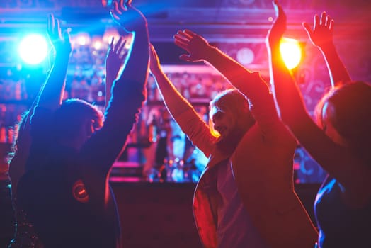 Happy friends with raised arms dancing at night club