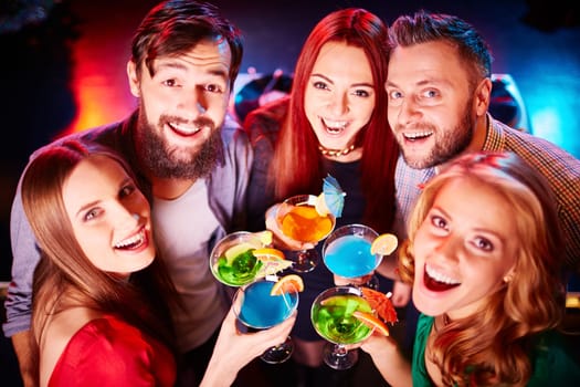 Ecstatic guys and girls toasting at party and looking at camera