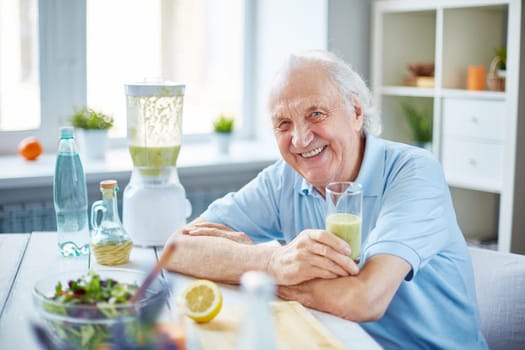 Senior man with glass of fruit smoothie sitting in the kitchen