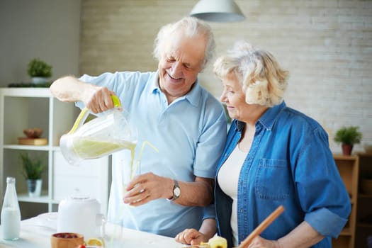 Senior man pouring healthy homemade fruit drink with his wife near by