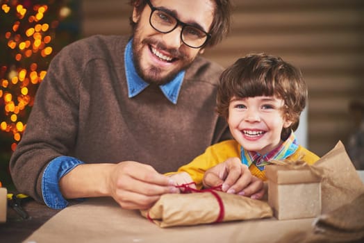 Young man and his son looking at camera with smiles while packing xmas gifts
