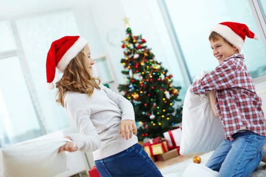 Playful kids in Santa caps having pillow fight