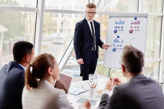 Happy young businessman pointing at chart on board while presenting review of marketing analysis