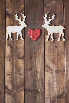 Toy reindeers with heart between them on wooden background