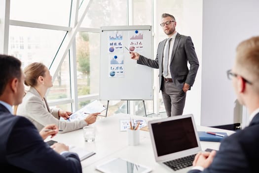 Experienced businessman by whiteboard looking at camera while presenting his review of financial analysis