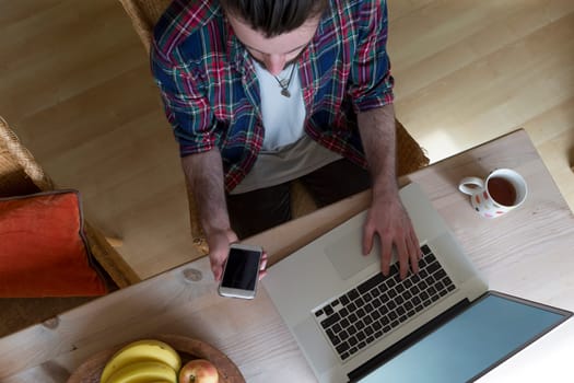 Ariel view of a young man using a laptop and smartphone