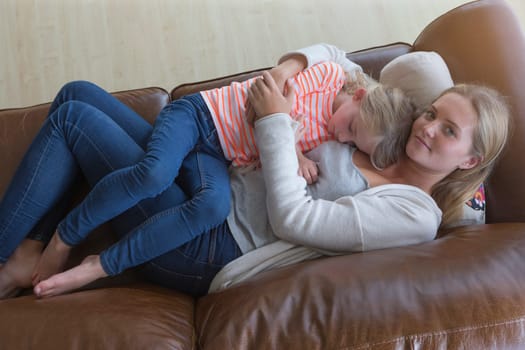 Ariel view of a mother cuddling her tired daughter on a sofa at home.