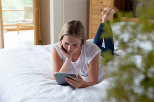 Woman lying on her bed at home using a digital tablet