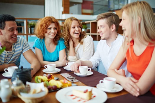 Happy friends relaxing and having tea with snack in cafe