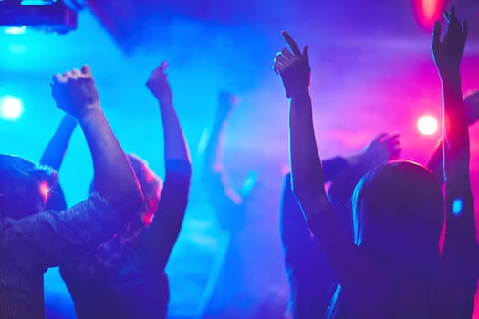 Group of dancing people with raised arms enjoying disco party