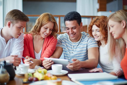 Modern teenage friends with touchpad sitting in cafe
