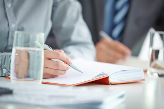 Female hand with pen writing working plan in notebook