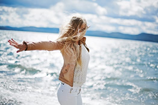 Happy long-haired girl standing with outstretched arms by the seaside