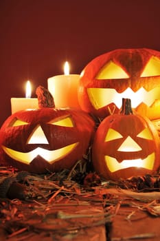 Three illuminated Halloween pumpkins with straw on old weathered wooden boards against a red background in candlelight
