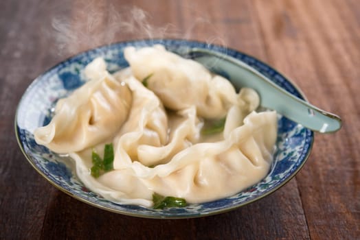 Fresh dumplings soup on plate with hot steams. Chinese dish on rustic old wooden background.