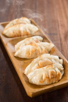 Fresh pan fried dumplings on plate with hot steams. Asian cuisine on rustic old vintage wooden background.