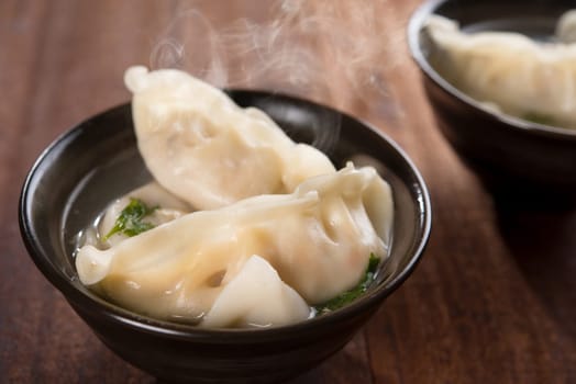 Fresh dumplings soup on plate with hot steams. Chinese gourmet on rustic old vintage wooden background.