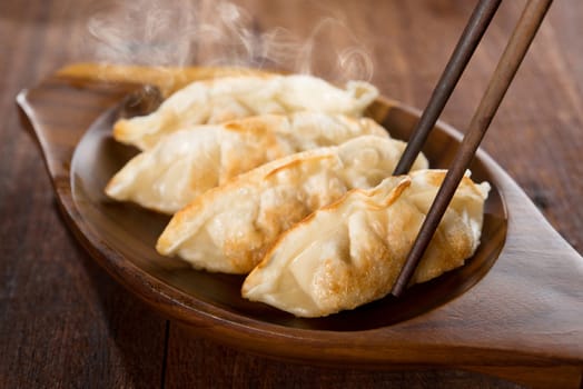Close up fresh pan fried dumplings on plate with chopsticks and hot steams. Asian food on old rustic vintage wooden background.