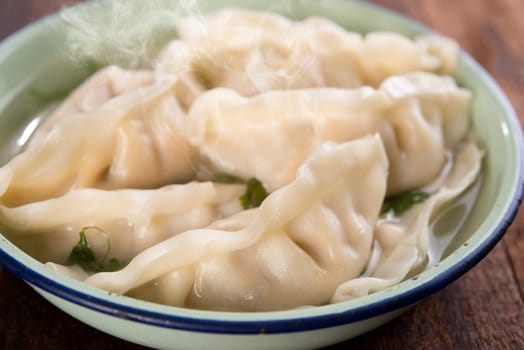 Close up fresh dumplings soup on plate with hot steams. Chinese gourmet on old vintage wooden background.