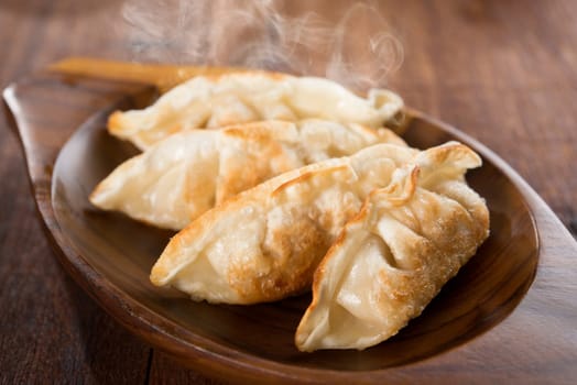 Fresh pan fried dumplings on plate with hot steams. Asian meal on rustic old vintage wooden background.