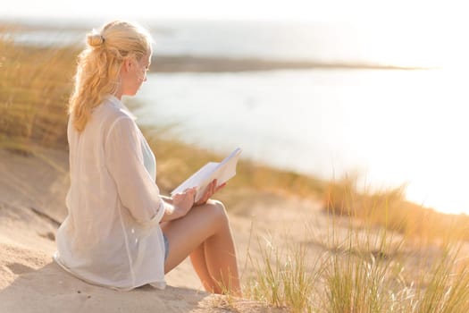 Relaxed woman enjoys reading on beautiful sandy beach.  Young lady with book in her hand. Concept of happiness, enjoyment and well being.  Enjoying Sun on Vacations.
