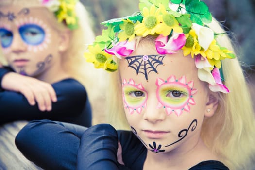 Little girls with black clothing and sugar skull makeup looking seriously at camera