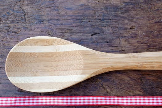 Cooking spoon on rustic wooden background with fabric ribbon