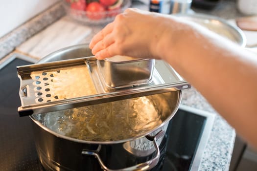 Hand makes Spätzle with a grater over a cooking pot