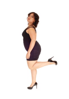 A young woman in a black dress standing in profile on one leg in a black.dress, isolated for white background..