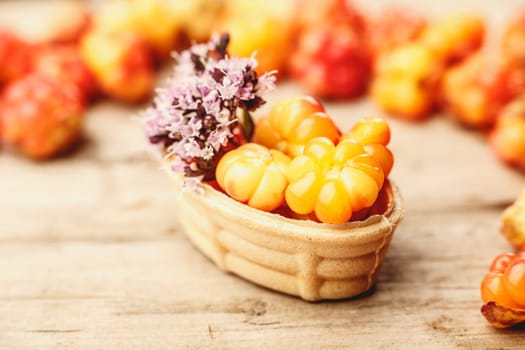 Cloudberry tart decorated with wild marjoram. Sweet baked dessert with fresh wild cloudberries on a wooden table.