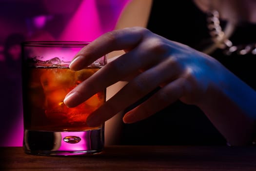 Woman's hand holding old fashioned glass with cold cocktail against blurred night club background