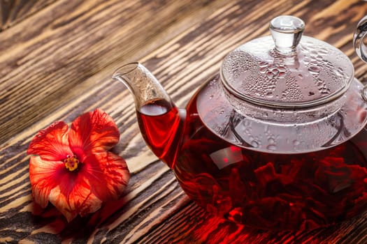 Hibiscus tea in transaprent teapot on wooden table. Worldwide popular healthy tea known as rosella, karkade or red sorrel.
