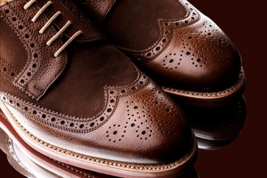 Unworn, laced pair of two tone men brogues (derbys) with elegant toe shape. The upper is stunning combination of brown calf with brown suede. Isolated on dark brown background with mirror reflection.