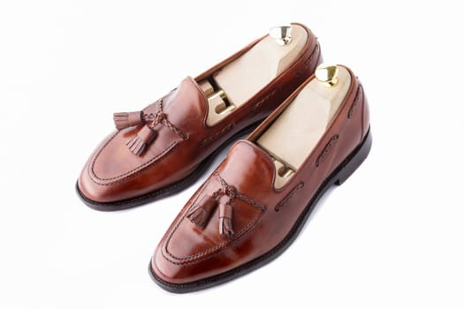 A pair of slightly worn, fine handcrafted tasseled vintage loafers with shoe trees inserted. Isolated on white background.