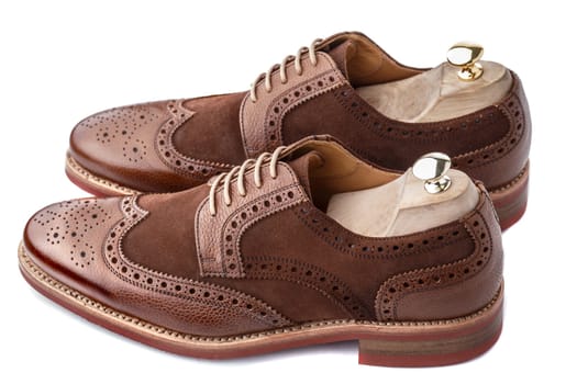 Unworn, laced pair of handcrafted shiny, two tone men brogues (also known as derbys, gibsons or wingtips) with shoe trees inserted on durable welted red brick rubber sole. The upper is stunning combination of brown calf with brown suede. Isolated on white background.