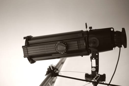 A theatre headlight stands on a railing and has been stabilized with several ropes and straps.